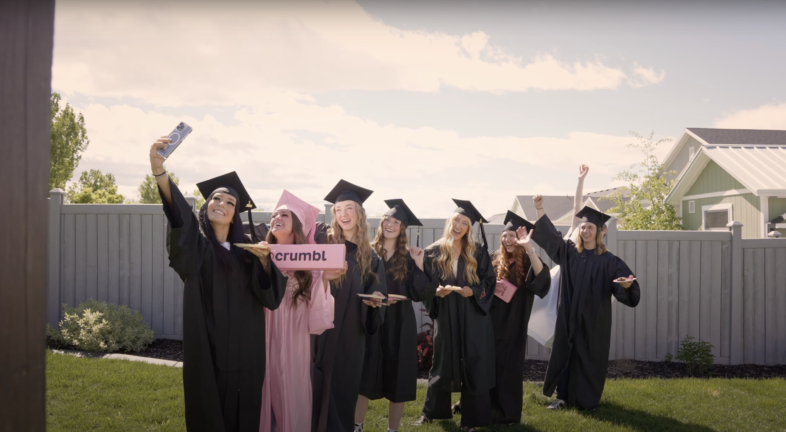 Graduates celebrating outdoors with a pink Crumbl box